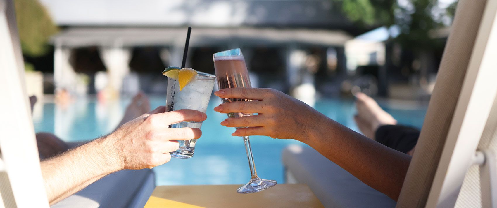 two women clinking cocktails glasses as they sit in chairs by the pool at Kimpton Sawyer Hotel